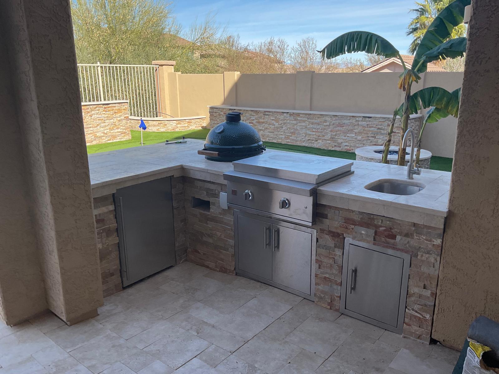 Custom stone outdoor kitchen with built-in grill, sink and ceramic smoker in an Arizona backyard