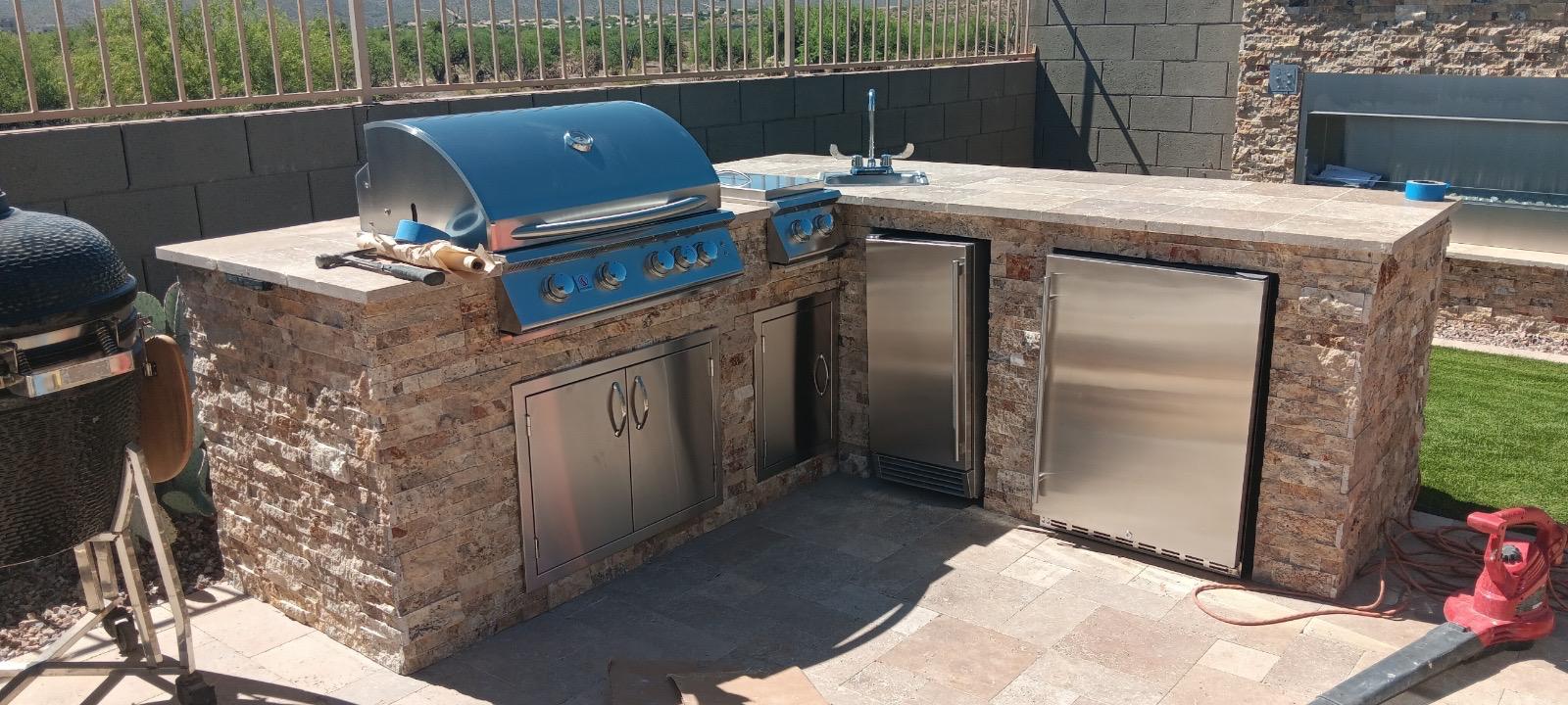 Large stone veneer outdoor BBQ island with grill, refrigerator and sink in an Arizona backyard