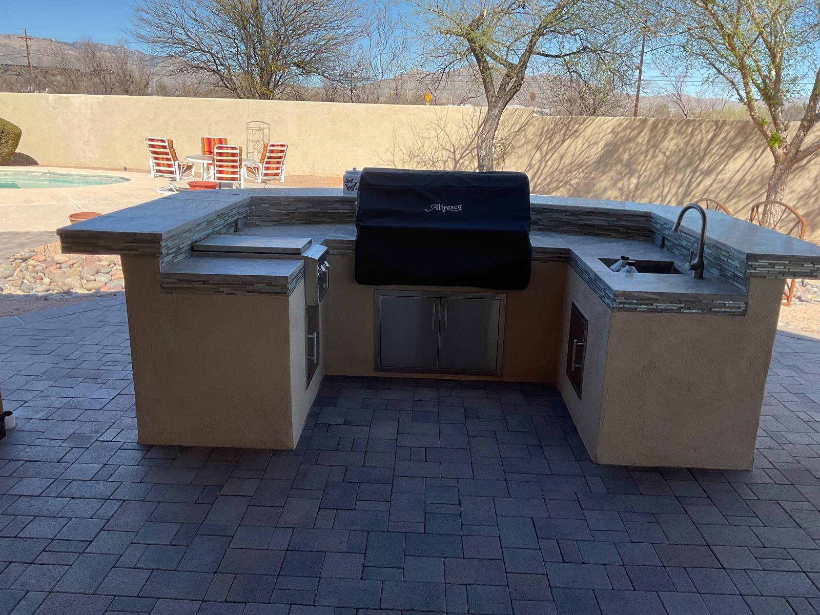 U-shaped outdoor kitchen with stone accents, built-in grill and sink beside an Arizona pool