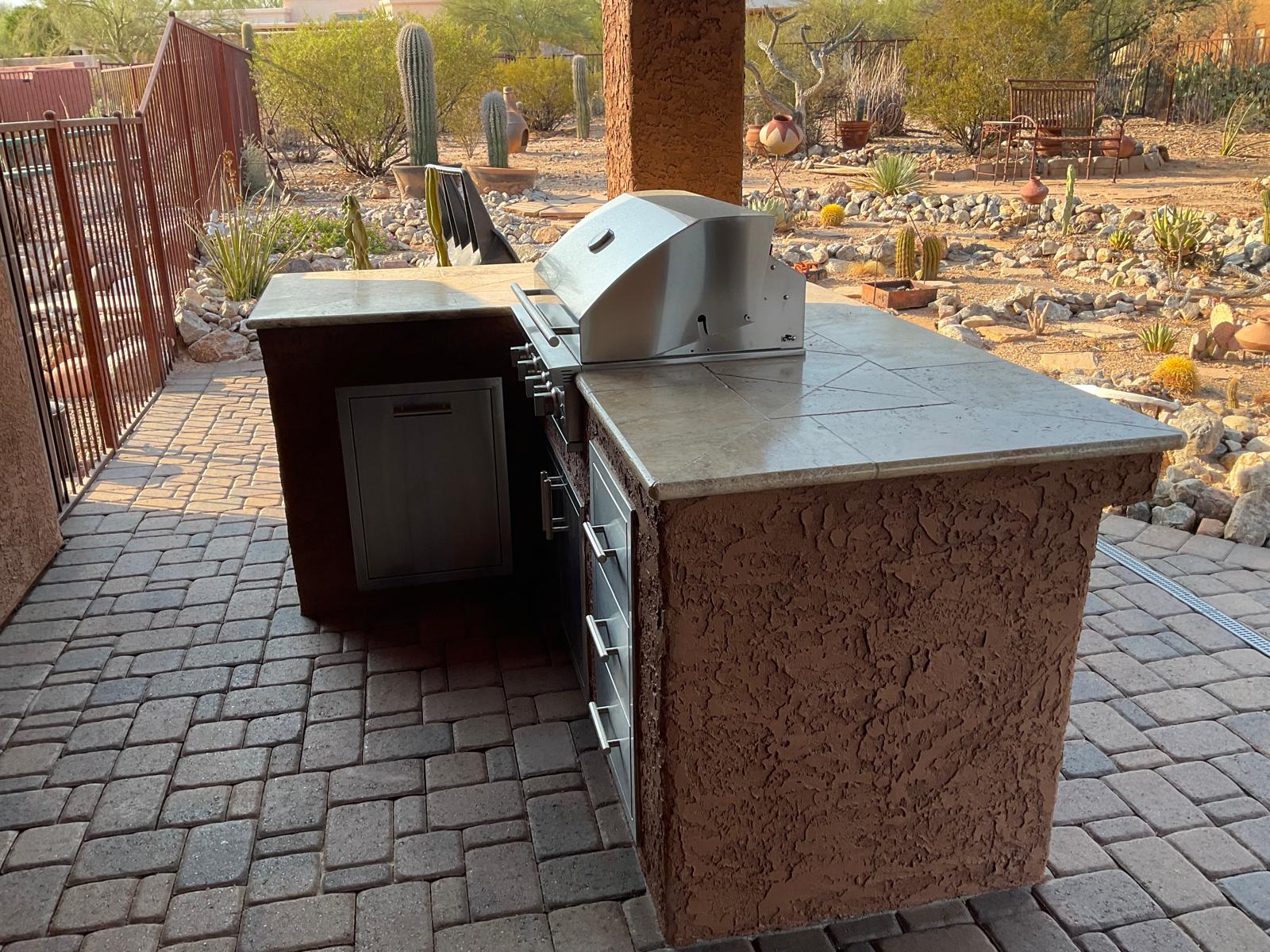 Built-in stainless steel barbecue grill island on a paver patio in an Arizona desert landscape