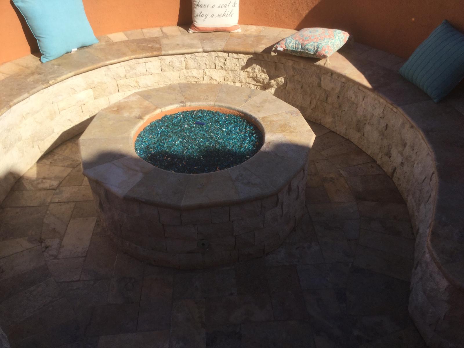 Custom stone fire pit with curved seating wall and glass beads in Arizona