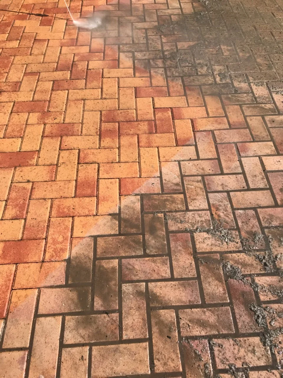 Close-up pressure washing orange-brown herringbone pavers in Phoenix Arizona