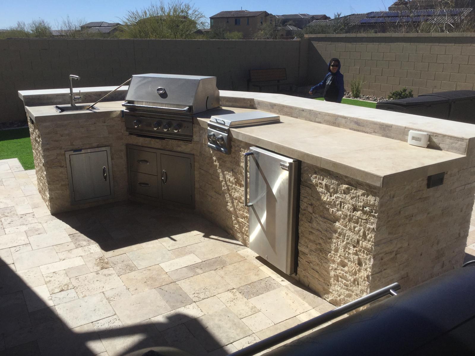 Stone outdoor kitchen with grill, side burner, sink and refrigerator in an Arizona backyard