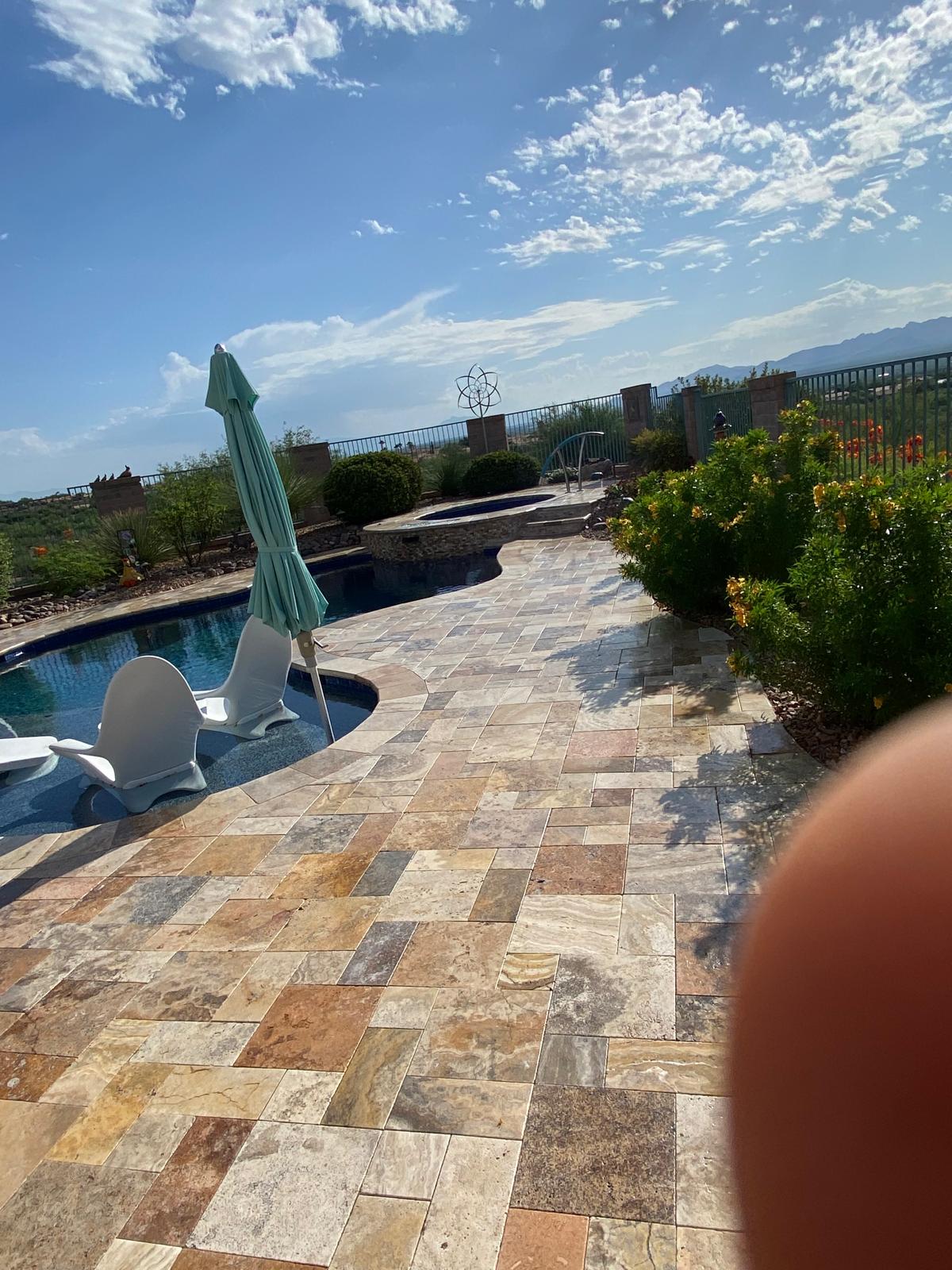 Sealed travertine pool deck with lounge chairs and umbrella in an Arizona backyard